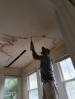 A man is using a drill to fix a ceiling in a room.