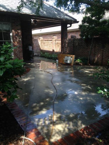 A patio is being cleaned with a pressure washer in front of a brick house.