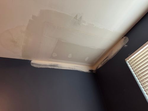 A room with a ceiling that is being painted and a window with blinds.