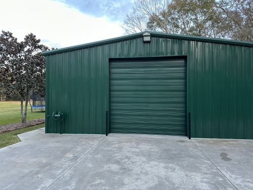 A green metal building with a garage door and a concrete driveway.