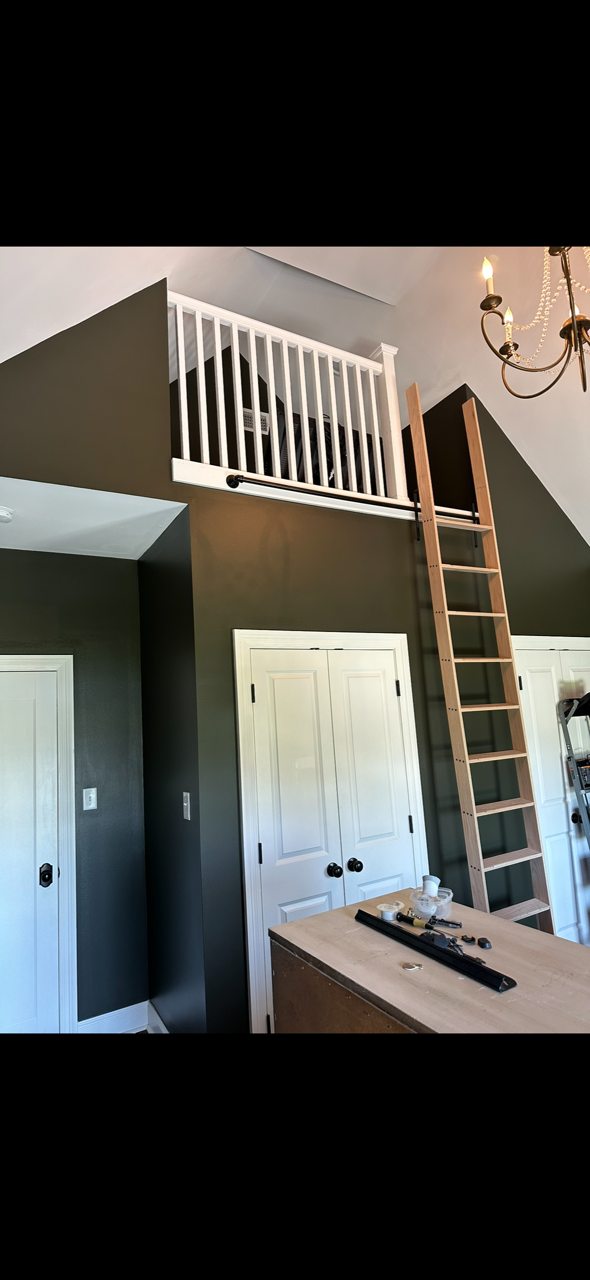 Loft with white railing, wooden ladder, and dark gray walls. Two white doors and a desk in the foreground.