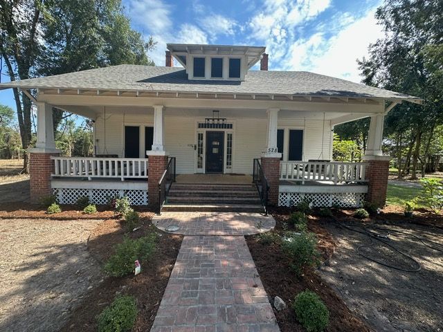White Craftsman-style house with porch, brick accents, and a brick walkway leading to the front door under a sunny sky.