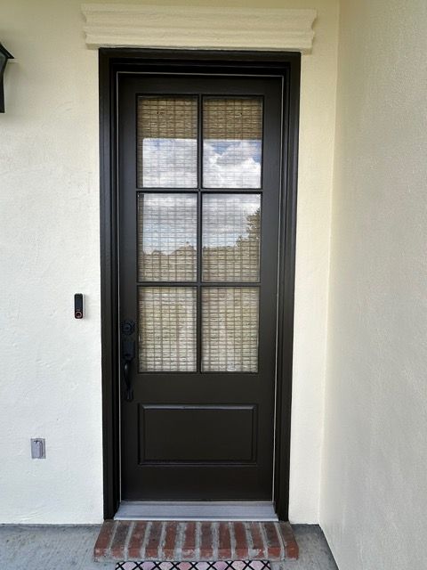 Dark brown front door with glass panels and woven shade, beige walls, and brick entry.