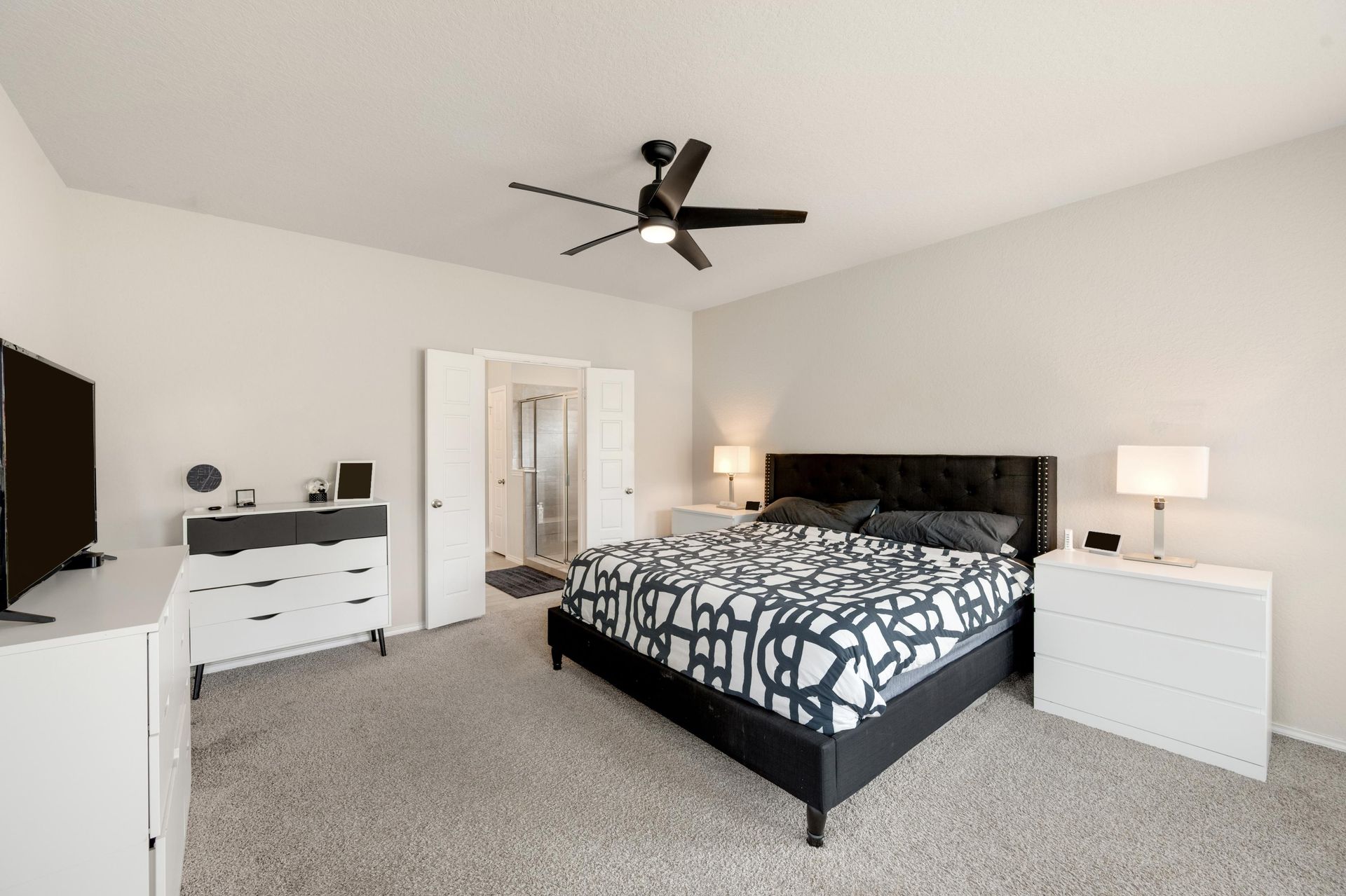 A bedroom with a bed , dresser , television and ceiling fan.
