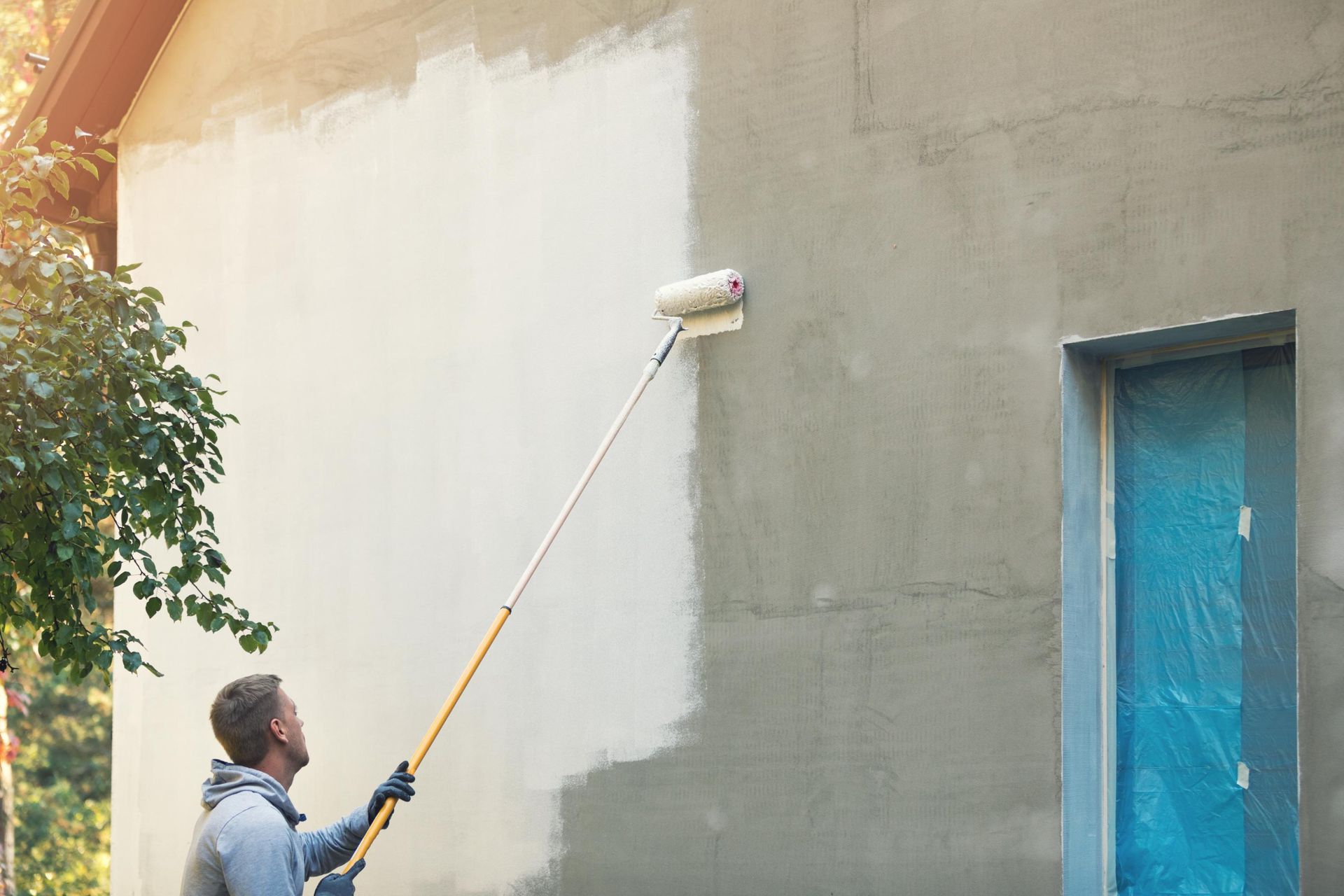 A man is painting the side of a building with a paint roller.