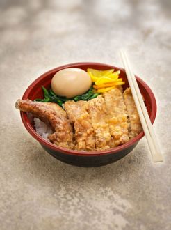 Japanese rice bowl with fried cutlet, egg, pickled garnish, and chopsticks