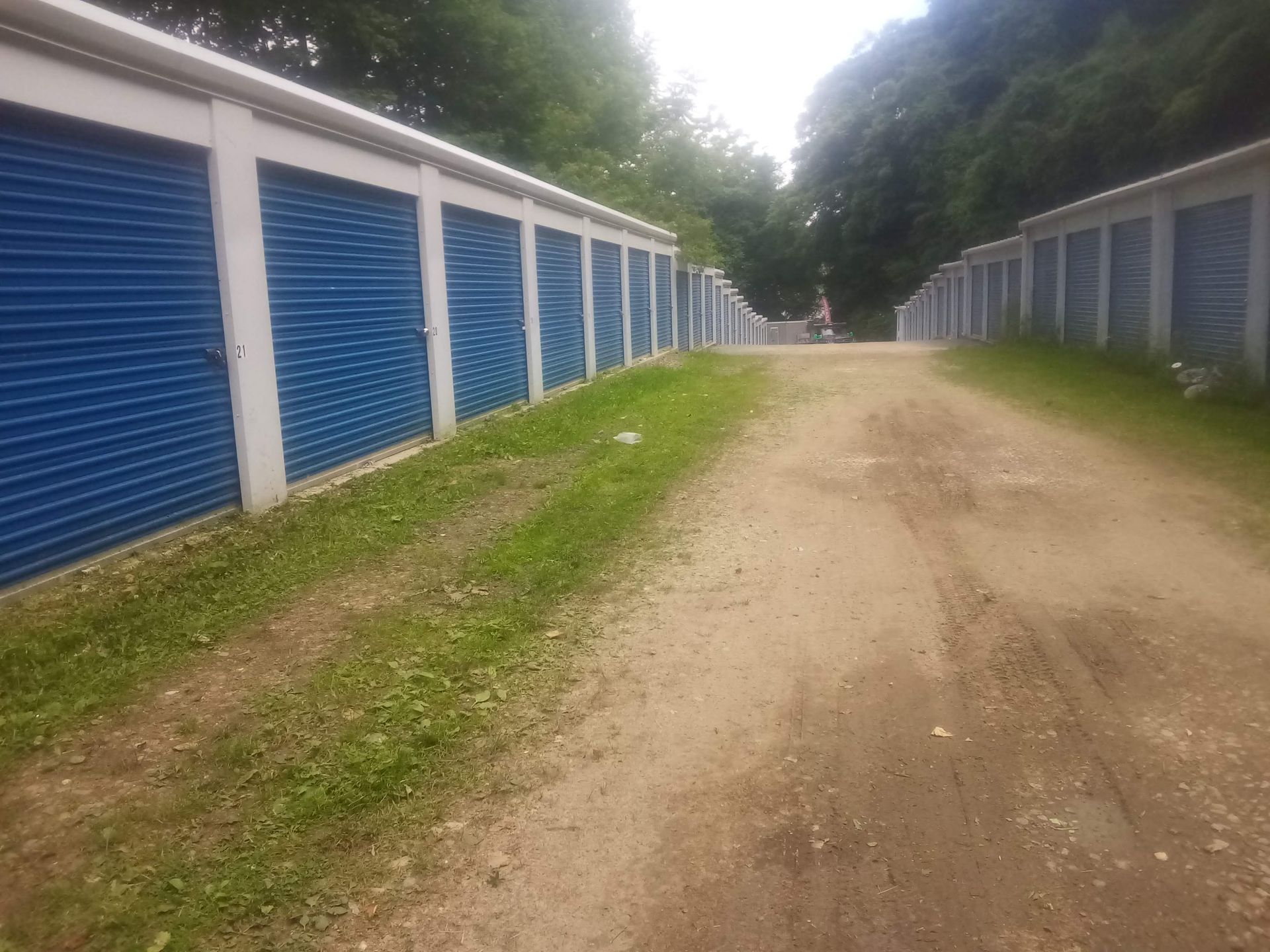 A dirt road leading to a row of blue garage doors.