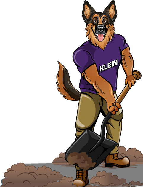 A german shepherd wearing a klein shirt is holding a blower