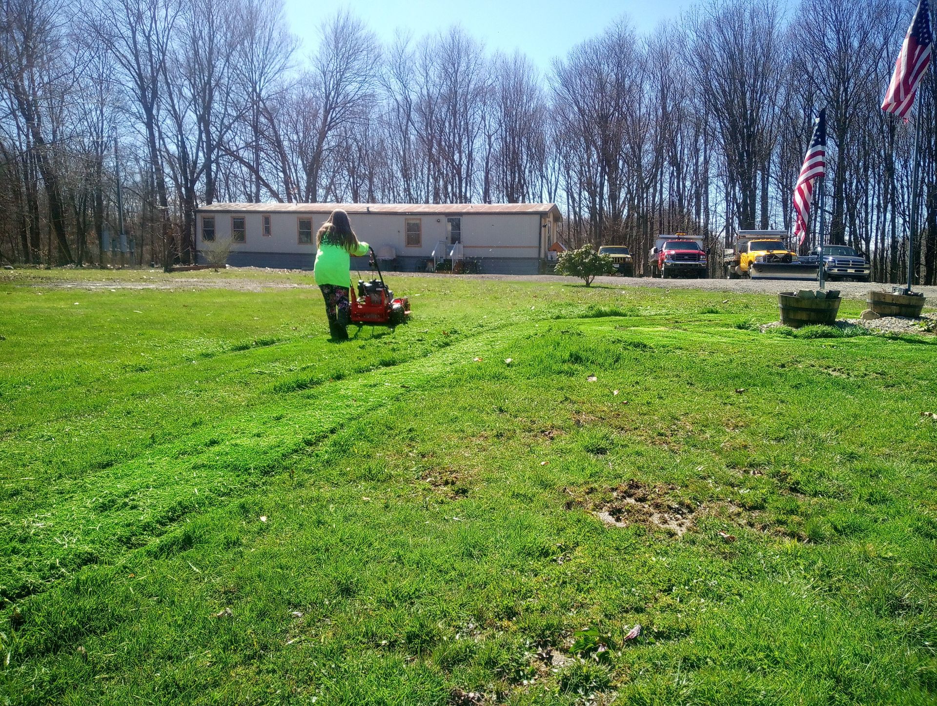 A person is mowing a lush green field with an american flag in the background.