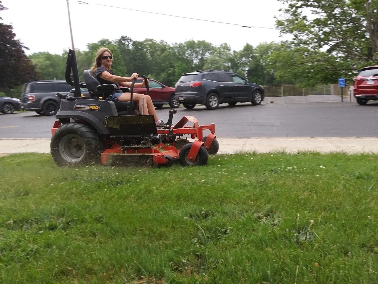 A woman is riding a lawn mower in a parking lot