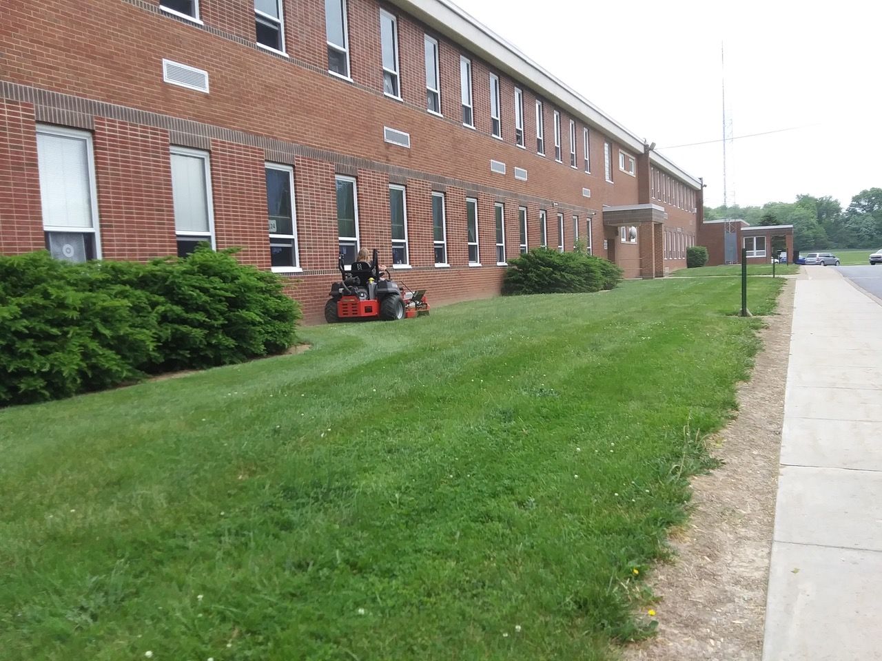 A person is mowing the grass in front of a large brick building