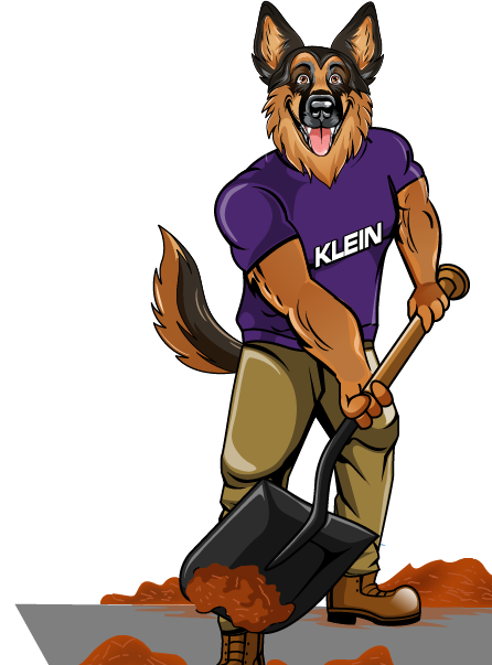 A german shepherd wearing a klein shirt is holding a blower
