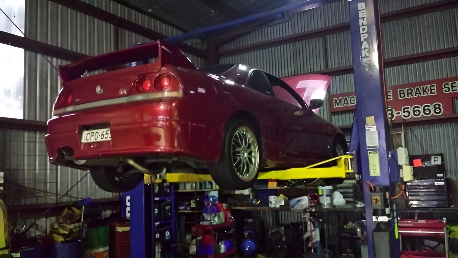 A Red Car is Sitting on a Lift in a Garage — Macquarie Brake & Automotive Services In Port Macquarie, NSW