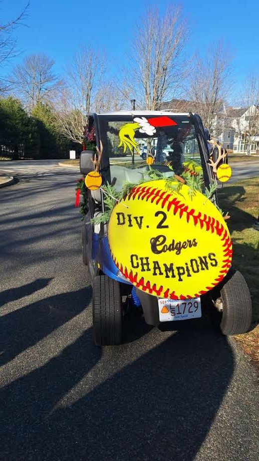 A decorated golf cart for a Div. 2 softball champions parade featuring a large yellow softball sign and Grinch ornaments.