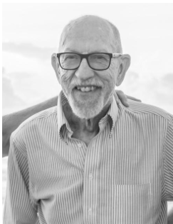 A smiling person wearing glasses and a striped button-down shirt, captured in a black-and-white portrait.