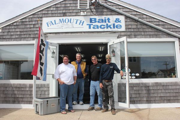 Four men stand in the doorway of Falmouth Bait & Tackle, a shingled storefront, with a large cooler nearby.