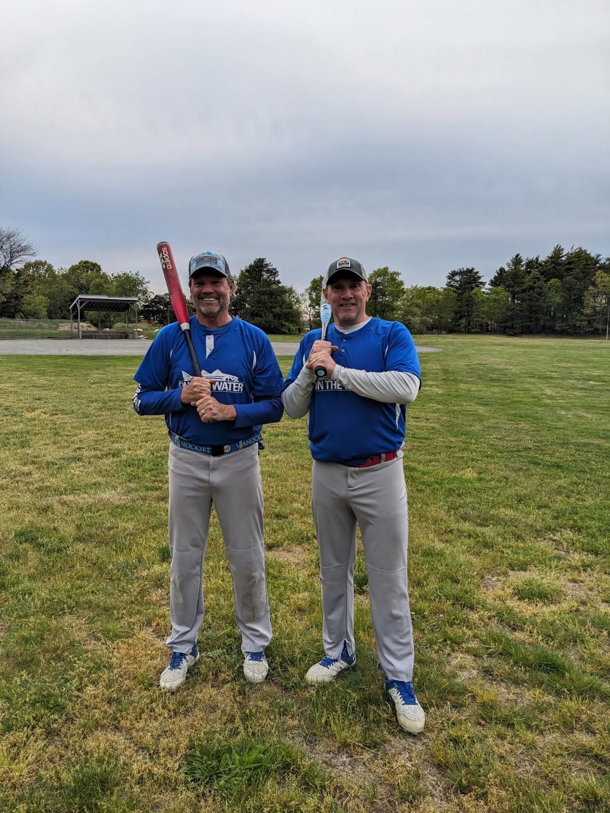 Two people pose on a gravel field, one holding a baseball glove, under a clear blue sky.