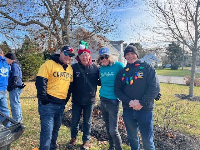 Four people stand together outdoors on a sunny day, posing for a photo while wearing casual winter clothing.