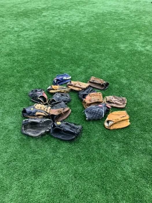 A cluster of several baseball gloves in various colors and sizes resting on a green artificial turf field.