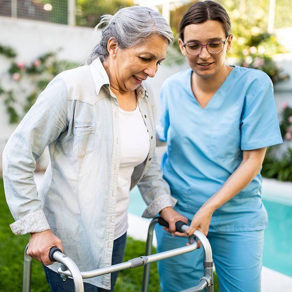 Caregiver assists an older woman with a walker outdoors near a pool