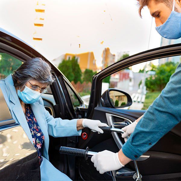 Masked attendant helping a masked passenger out of a car with open door