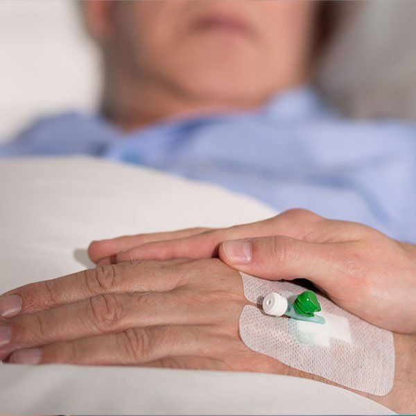 Hand resting on a hospital bed with IV tubing and a taped catheter line