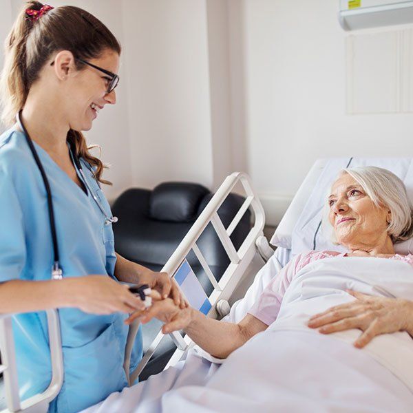 Nurse in blue scrubs holding hands with a smiling patient in a hospital bed