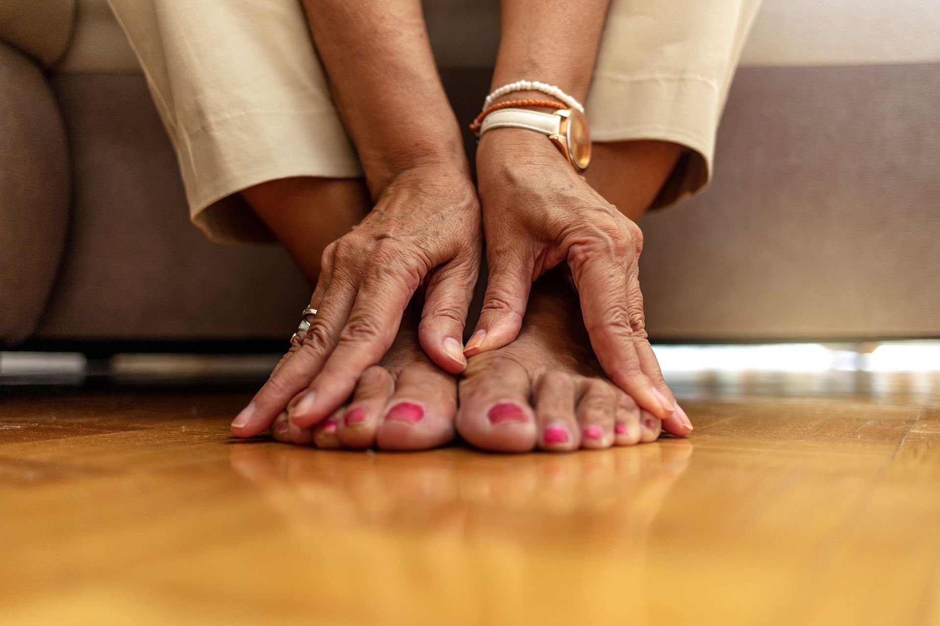 Hands with pink nail polish resting on a wooden floor near a sofa