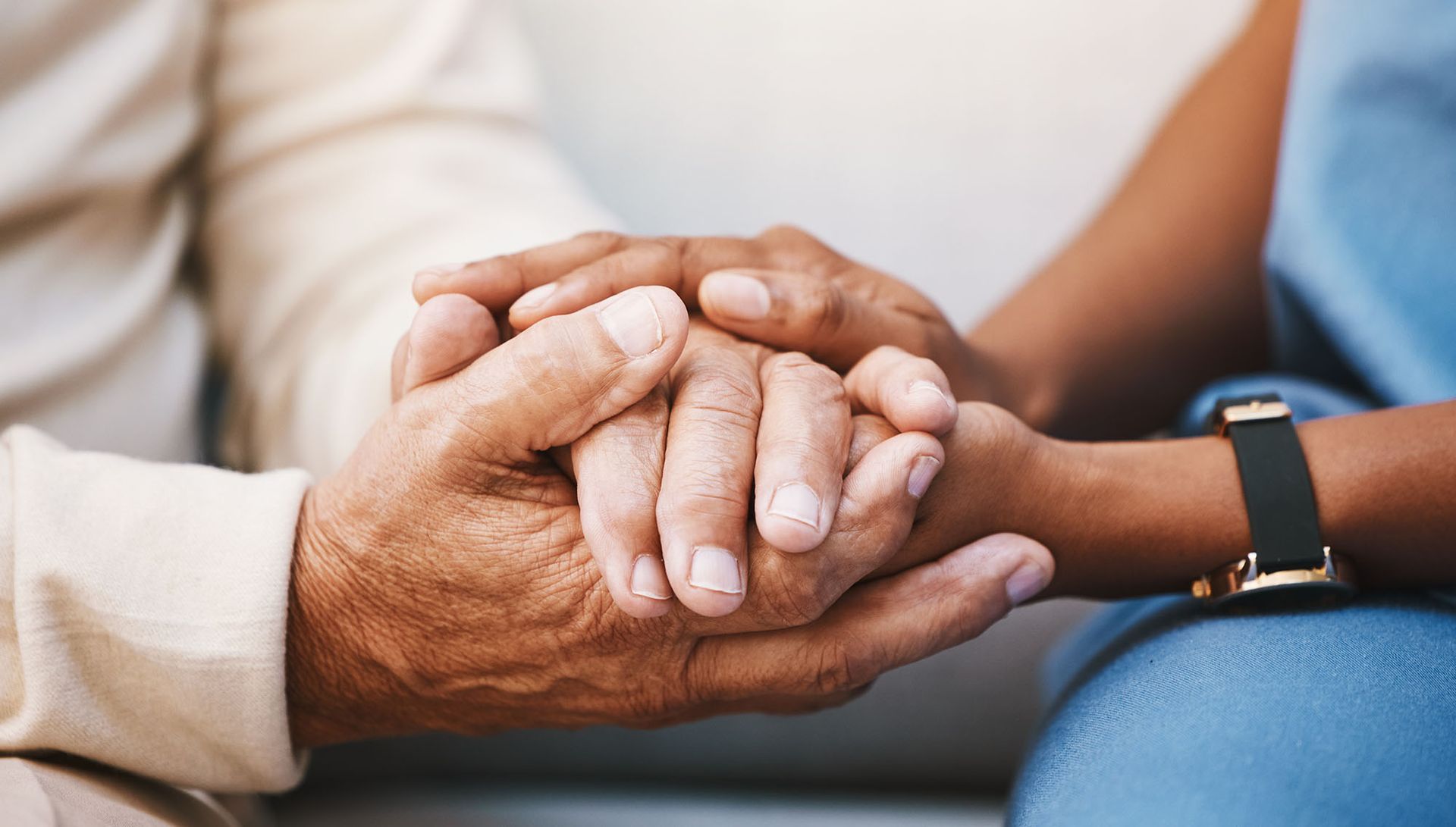 Two people holding hands in a supportive gesture, one wearing a blue smartwatch