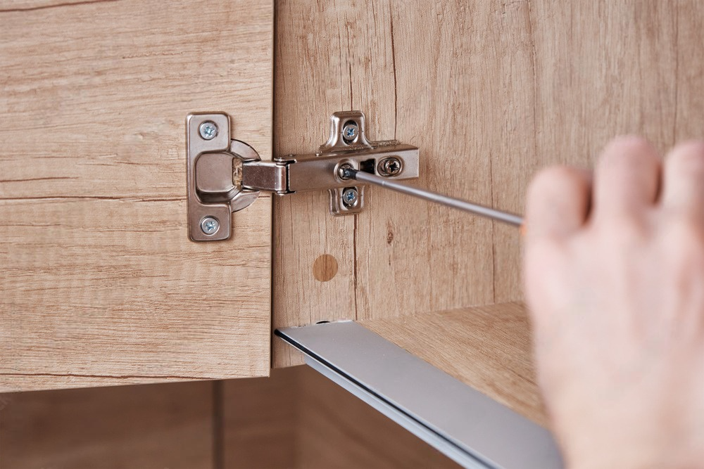 a person is fixing a cabinet door with a screwdriver .