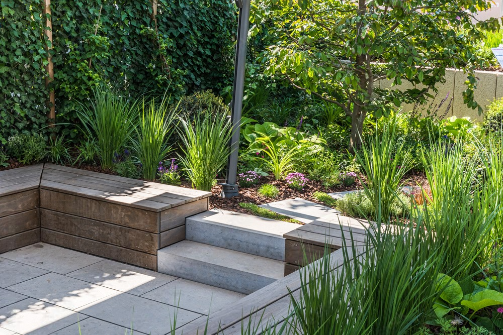 a garden with stairs leading up to a patio surrounded by plants and trees .