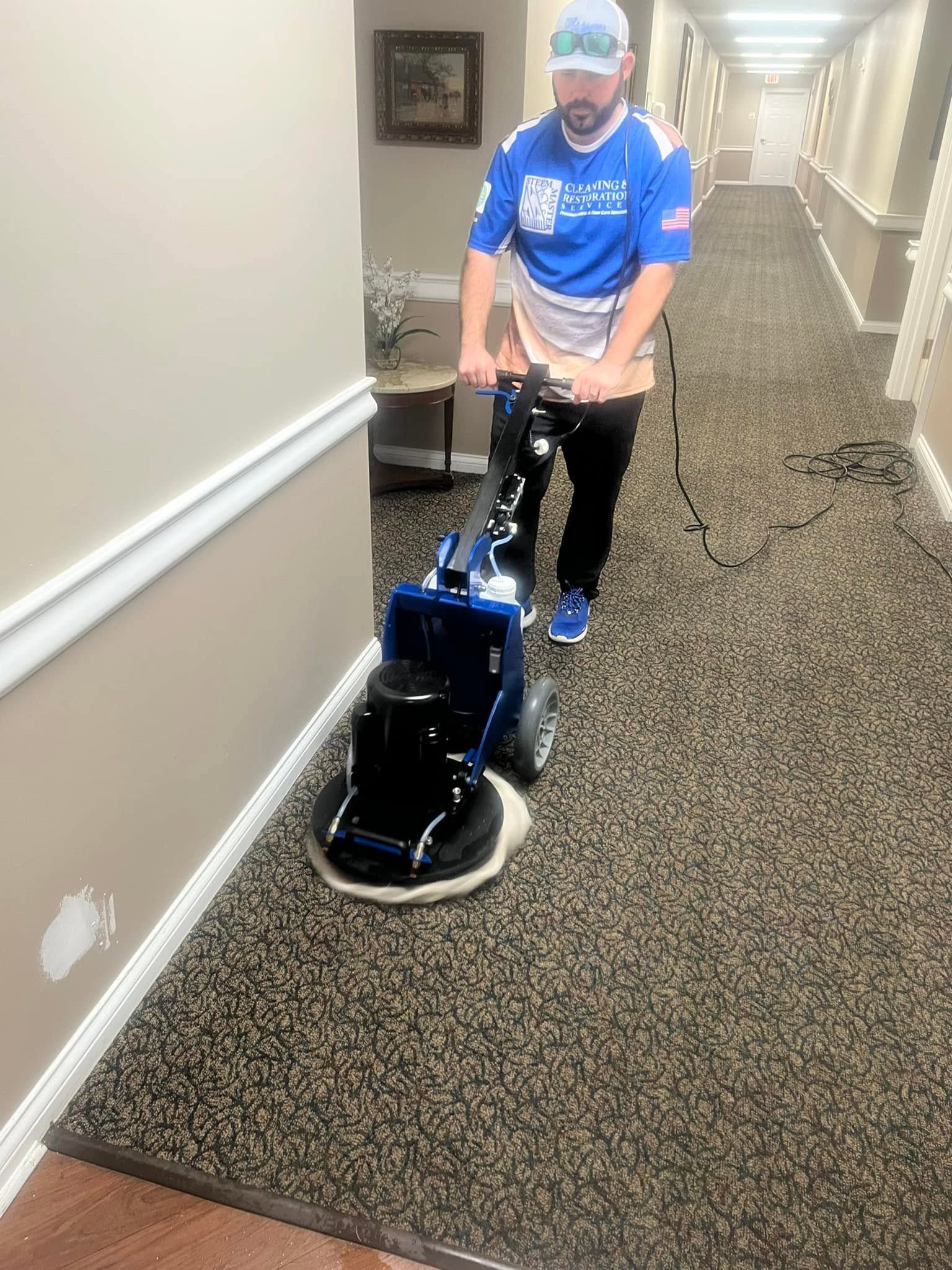 Worker using a floor-polishing machine in a carpeted hallway indoors