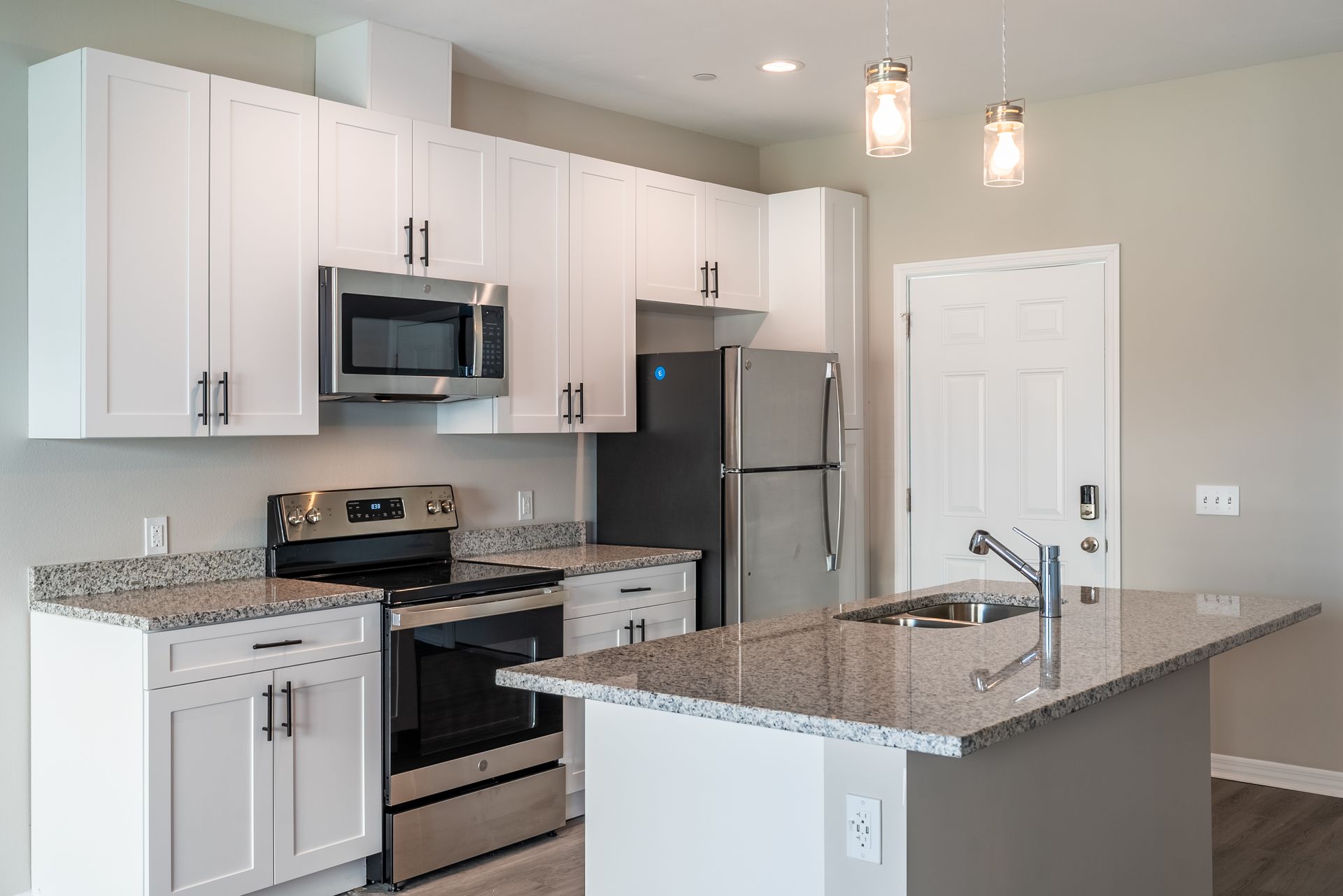 a kitchen with white cabinets , stainless steel appliances , granite counter tops and a large island