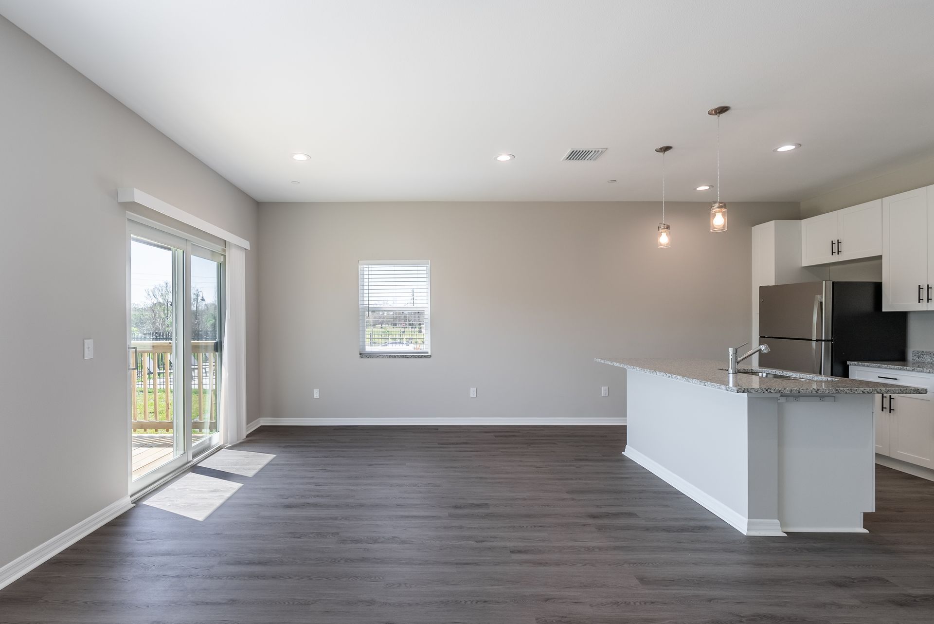 an empty living room with a kitchen and sliding glass doors