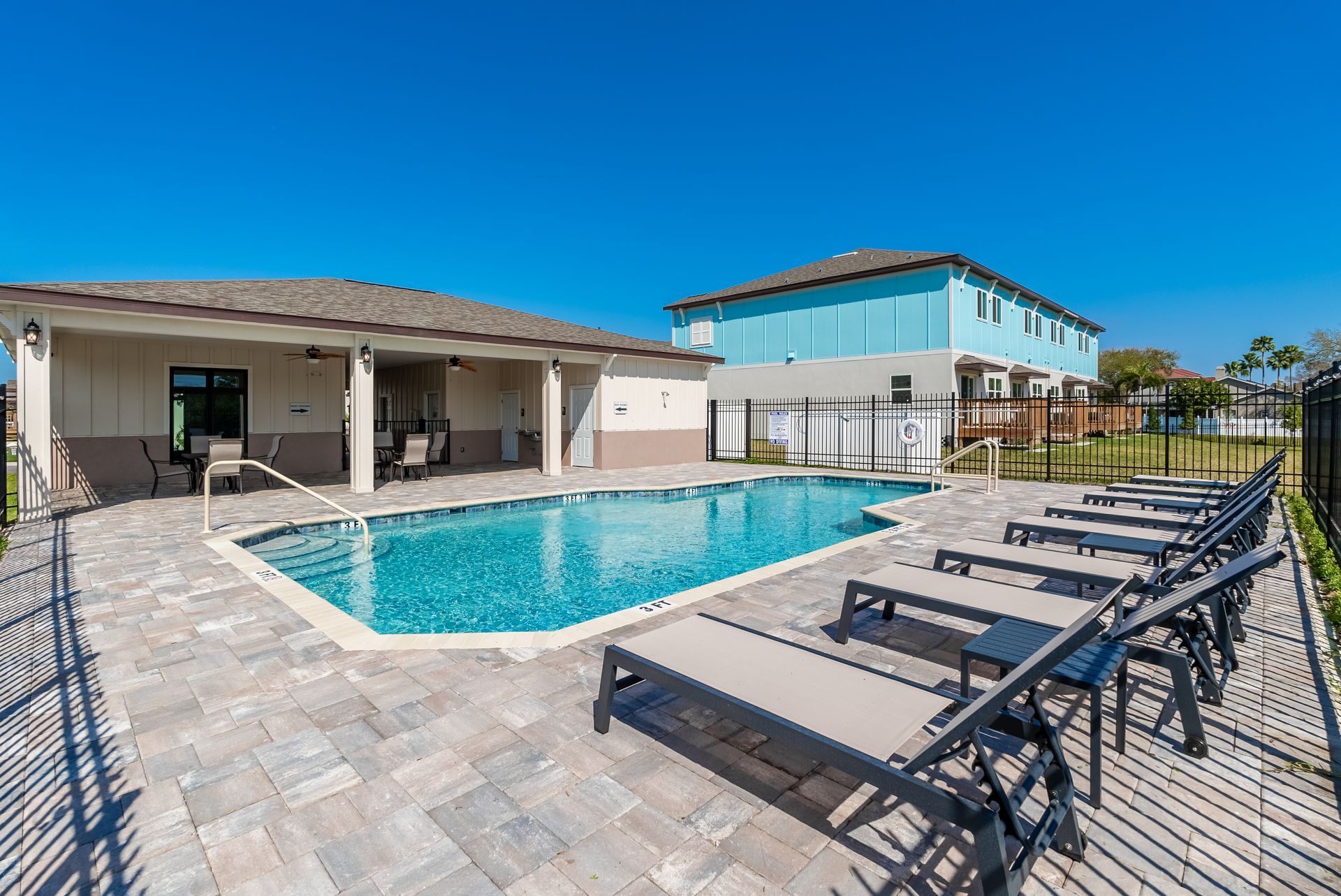 a large swimming pool surrounded by lounge chairs in front of a clubhouse at Whitney Place Townhomes