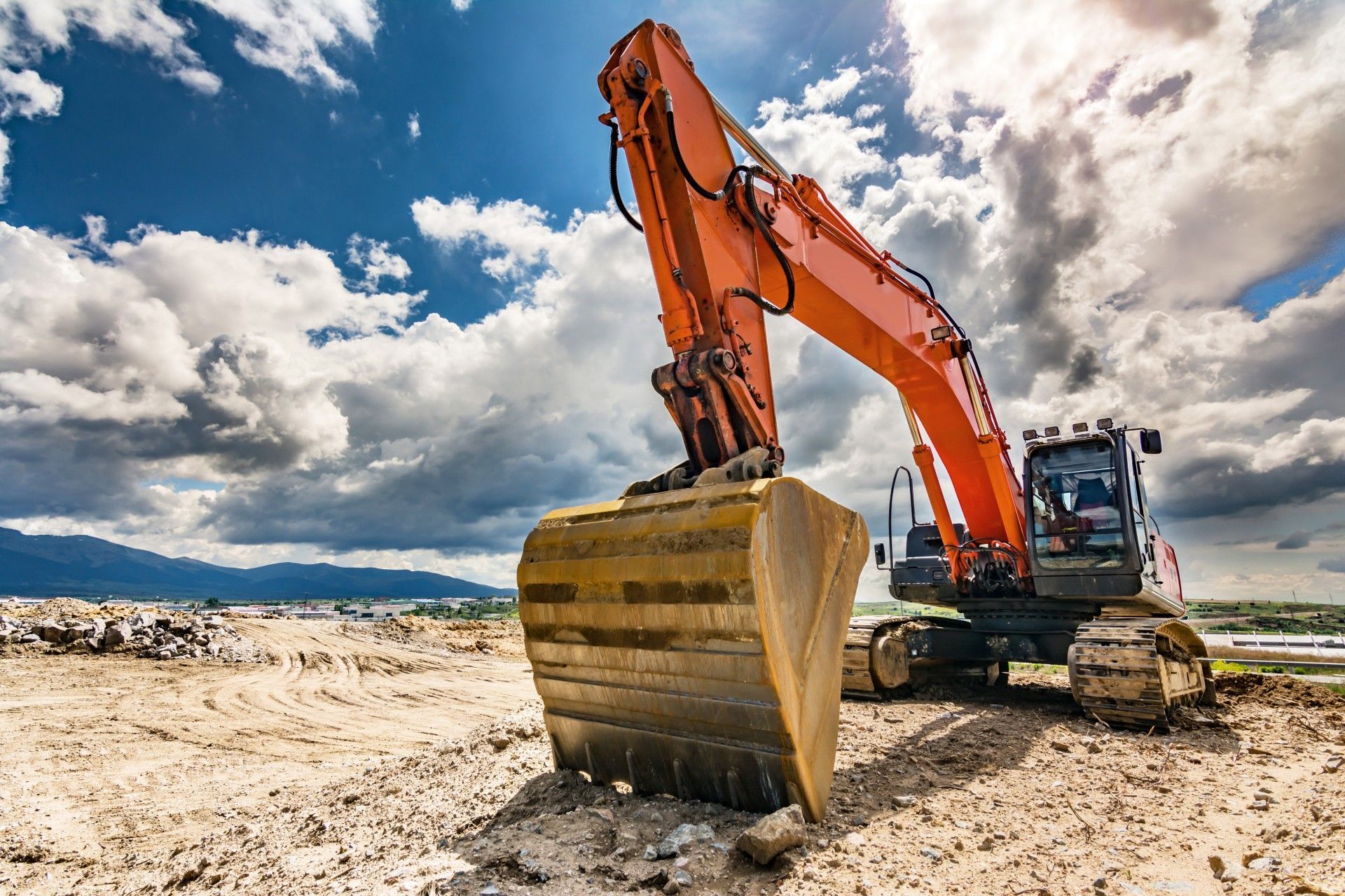 A large orange excavator is sitting on top of a dirt field.