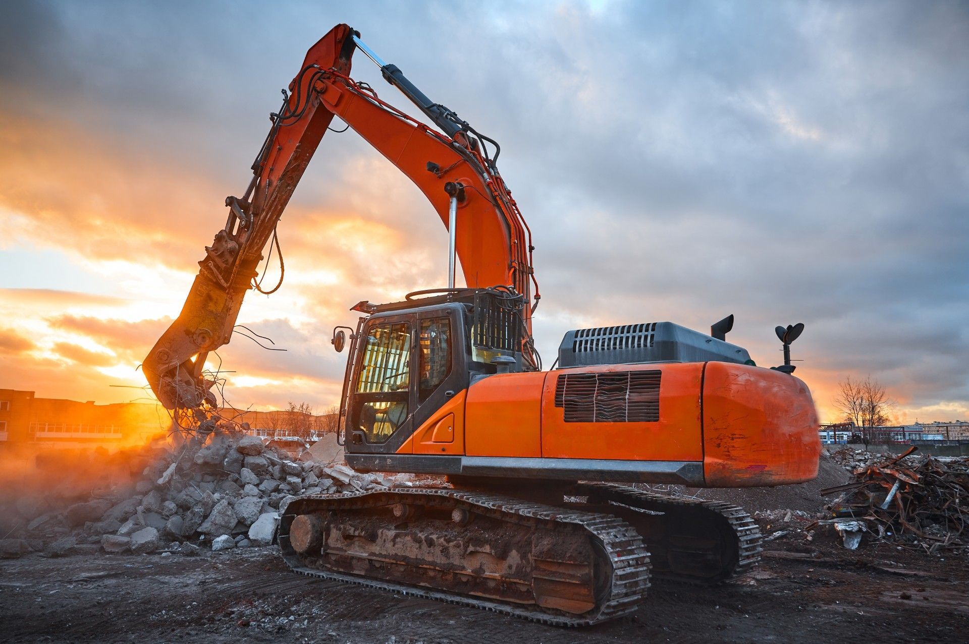 A large orange excavator is working on a construction site at sunset.