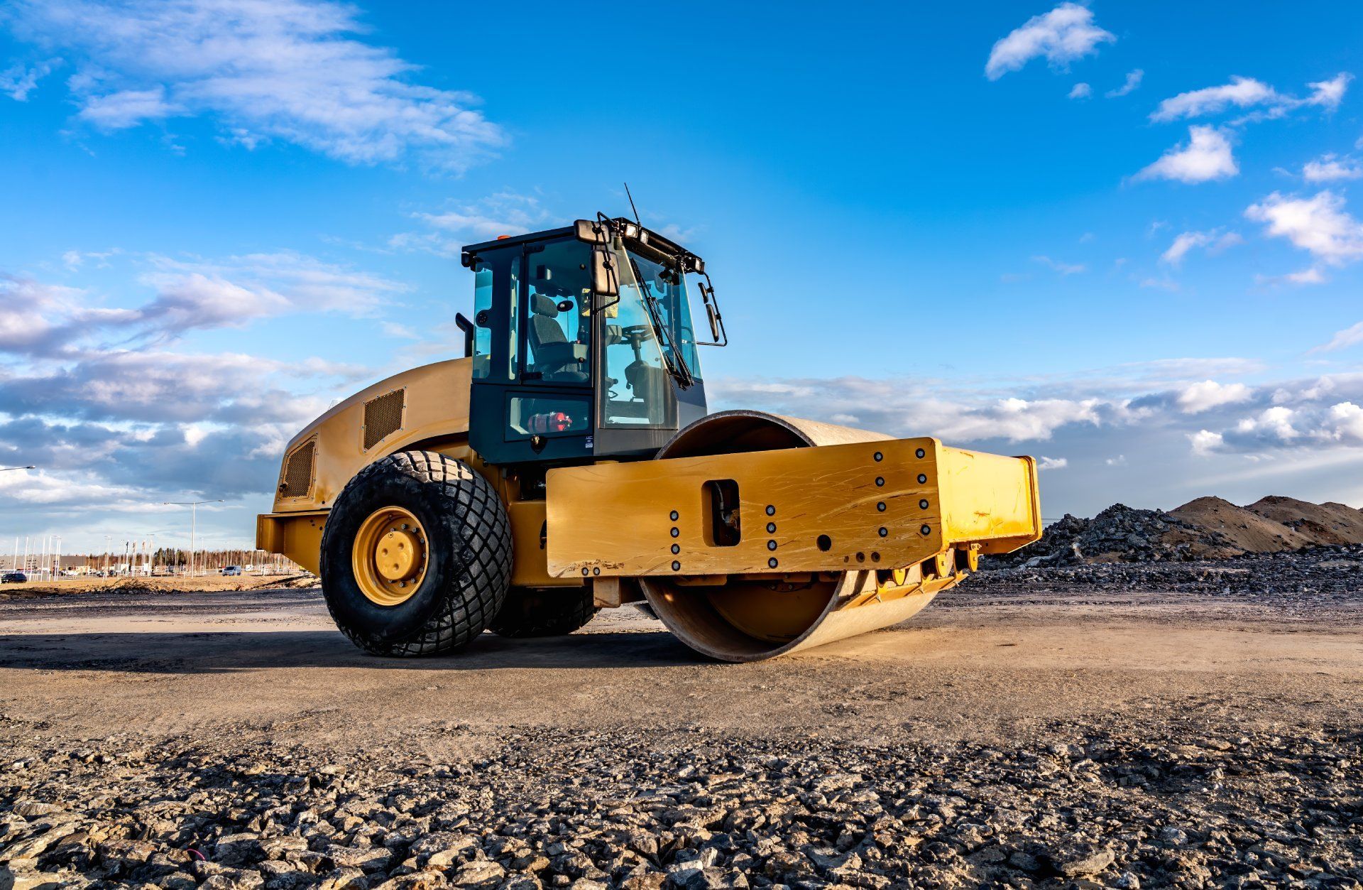 A yellow road roller is sitting on top of a dirt field.