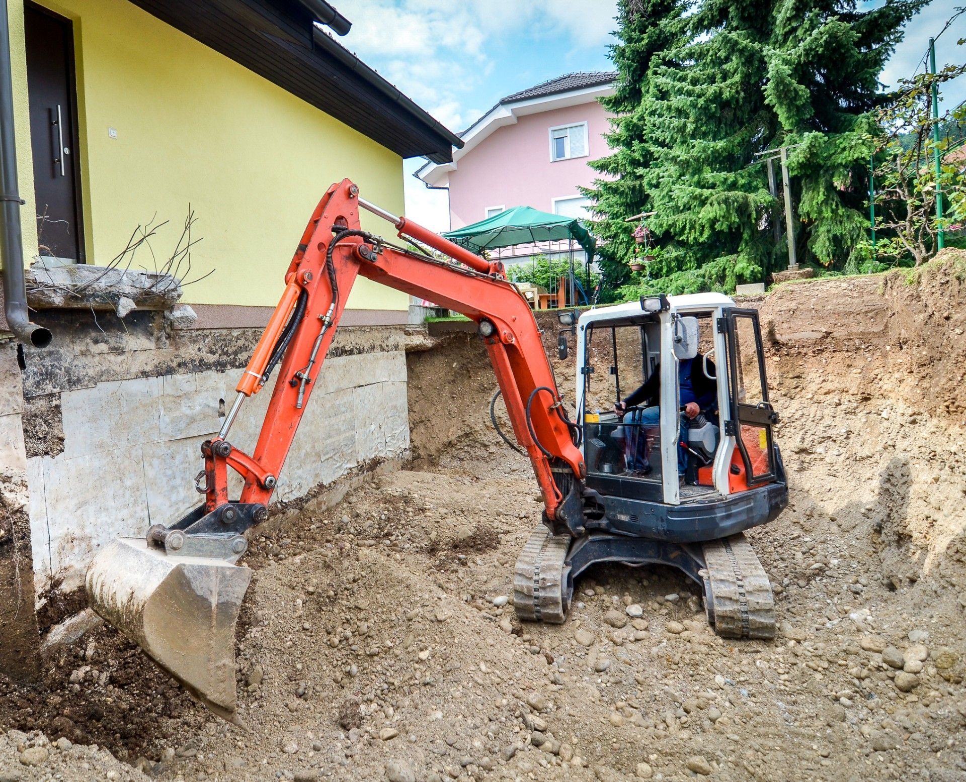 An excavator is digging a hole in front of a house.