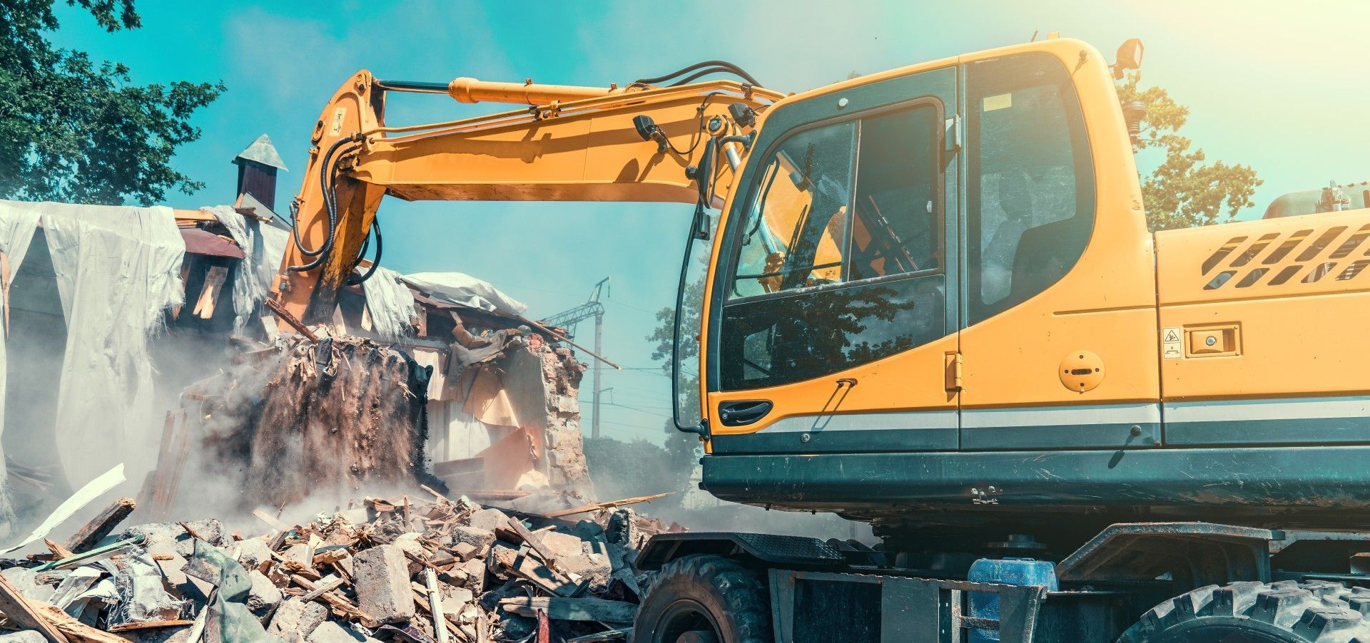 A yellow excavator is demolishing a building on a construction site.
