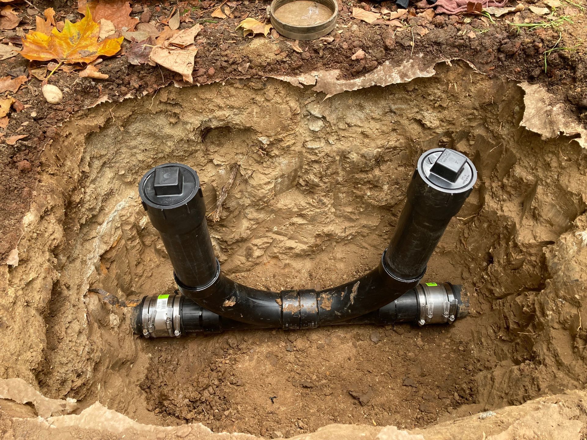 A black pipe is sitting in the dirt in a hole.