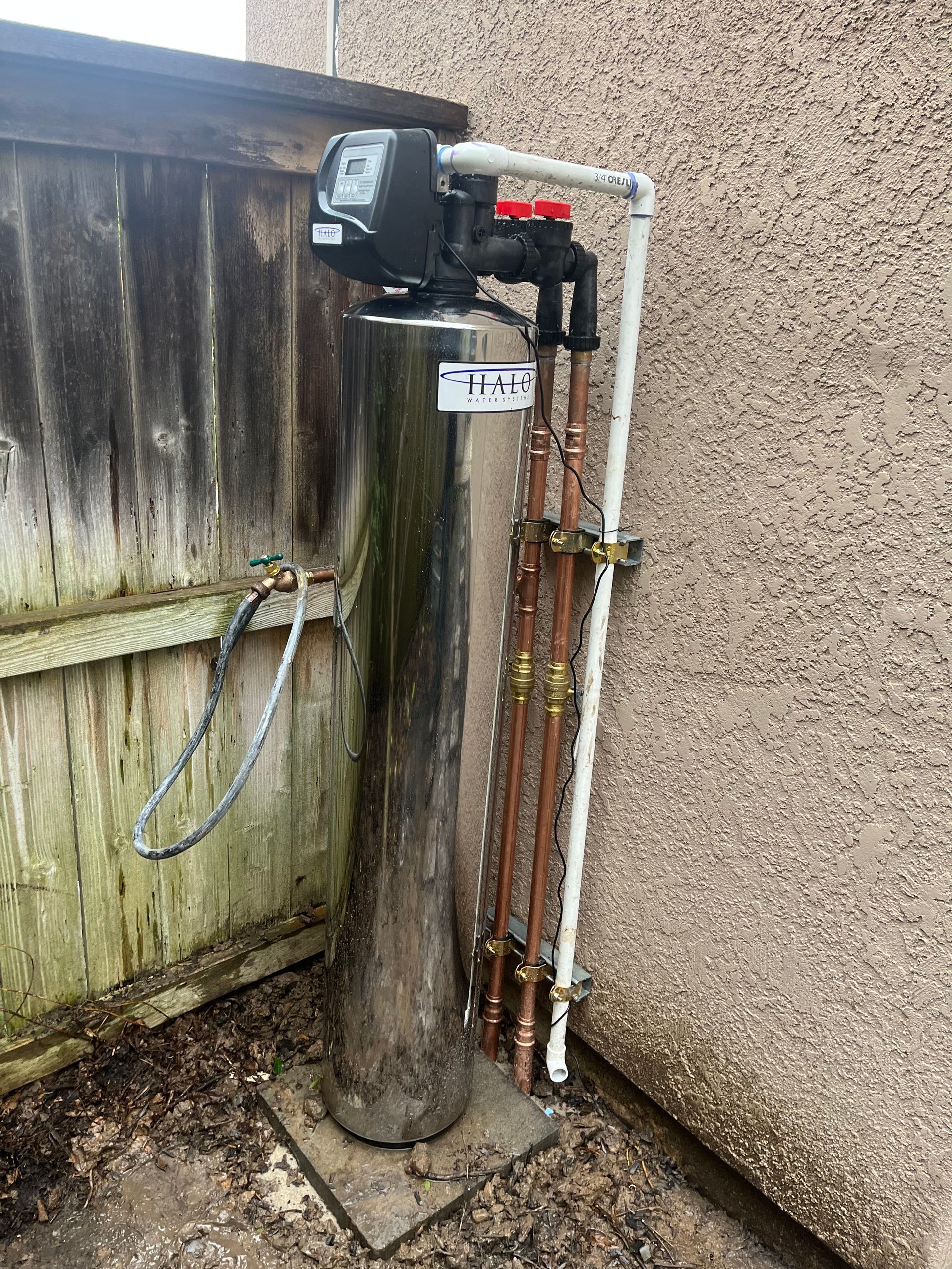 A water filter is sitting on the side of a building next to a fence.