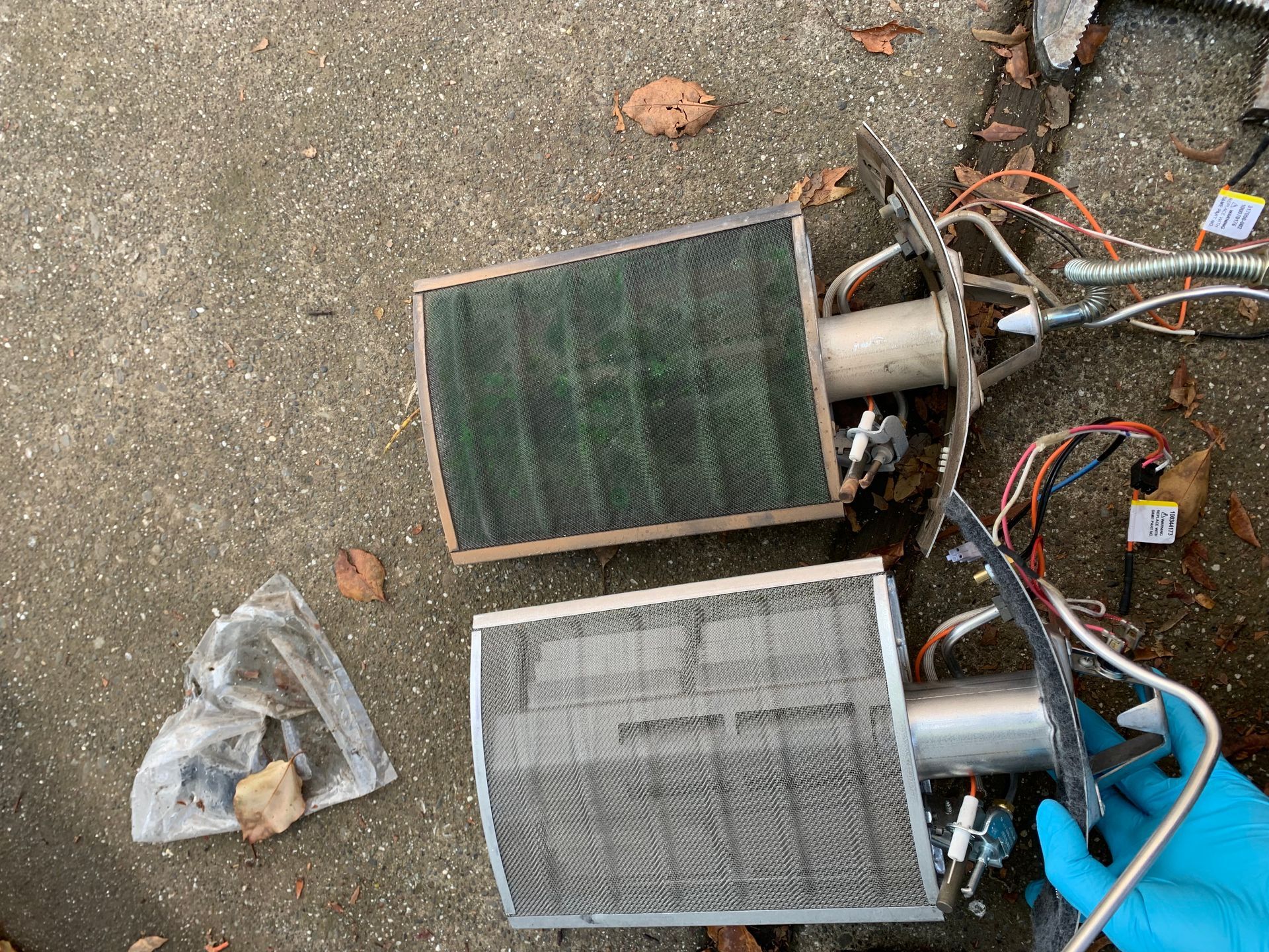 A person wearing blue gloves is holding a pair of burners on the ground.