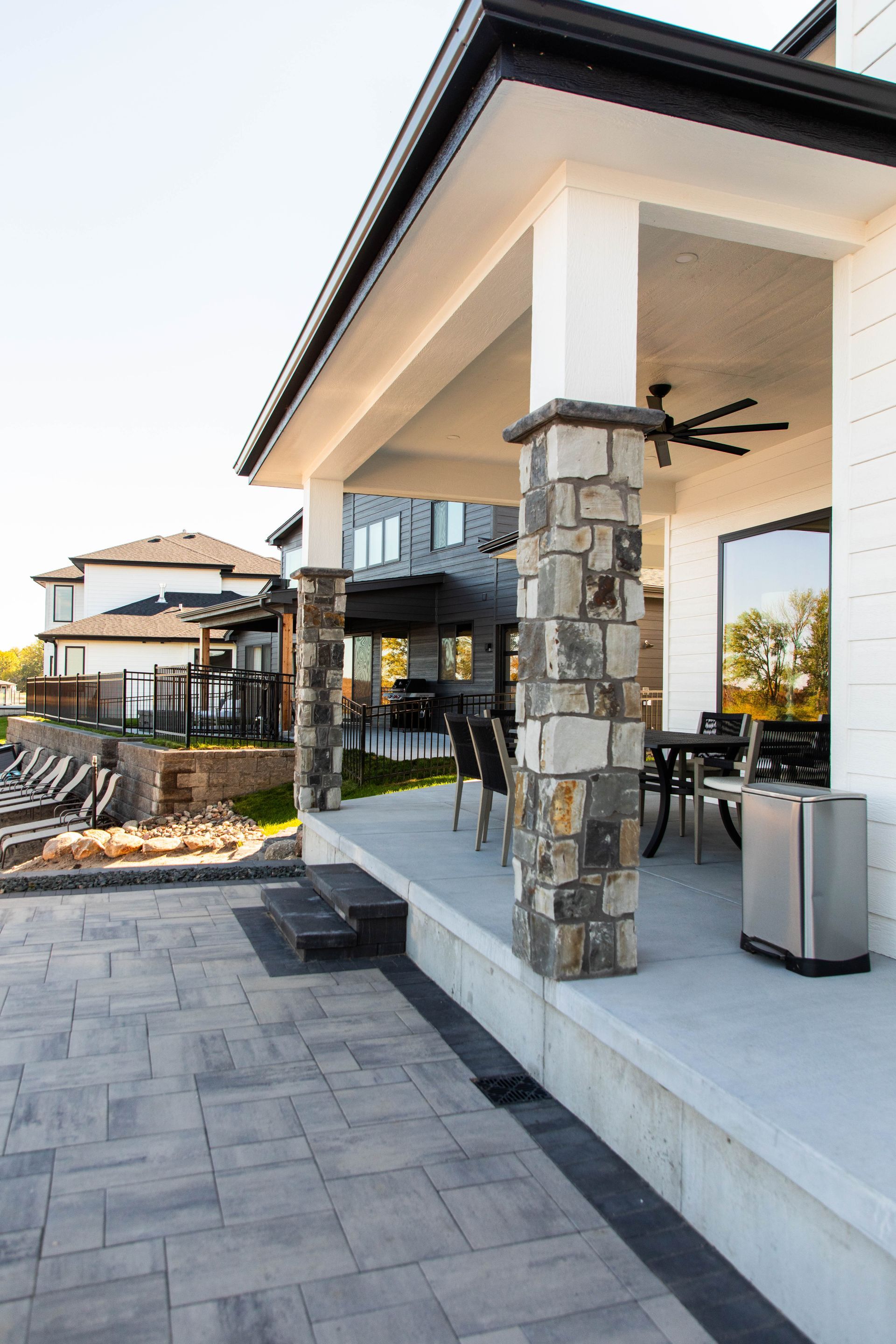 A patio with a ceiling fan and a trash can in front of a house.