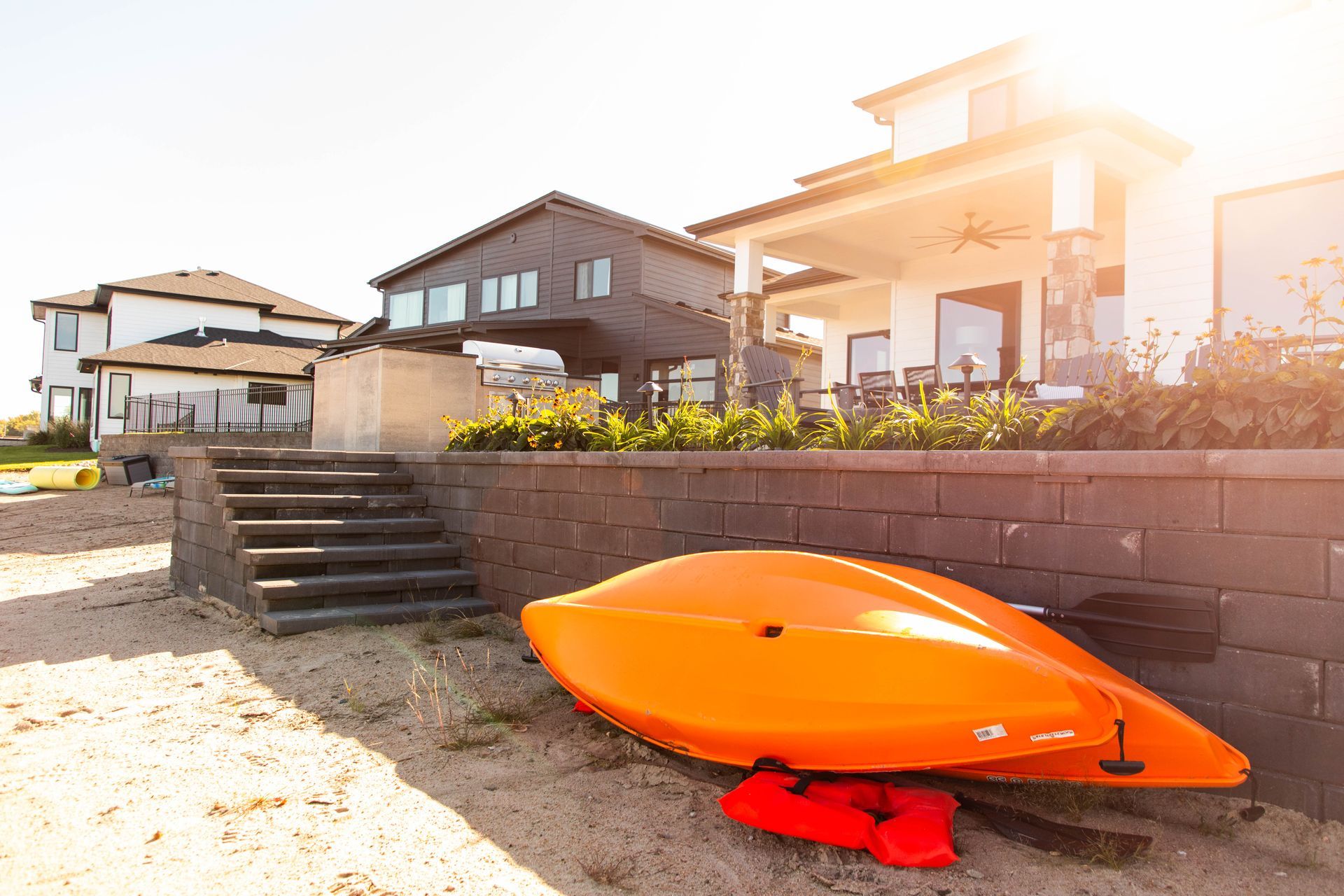 An orange kayak is sitting on the beach in front of a house.