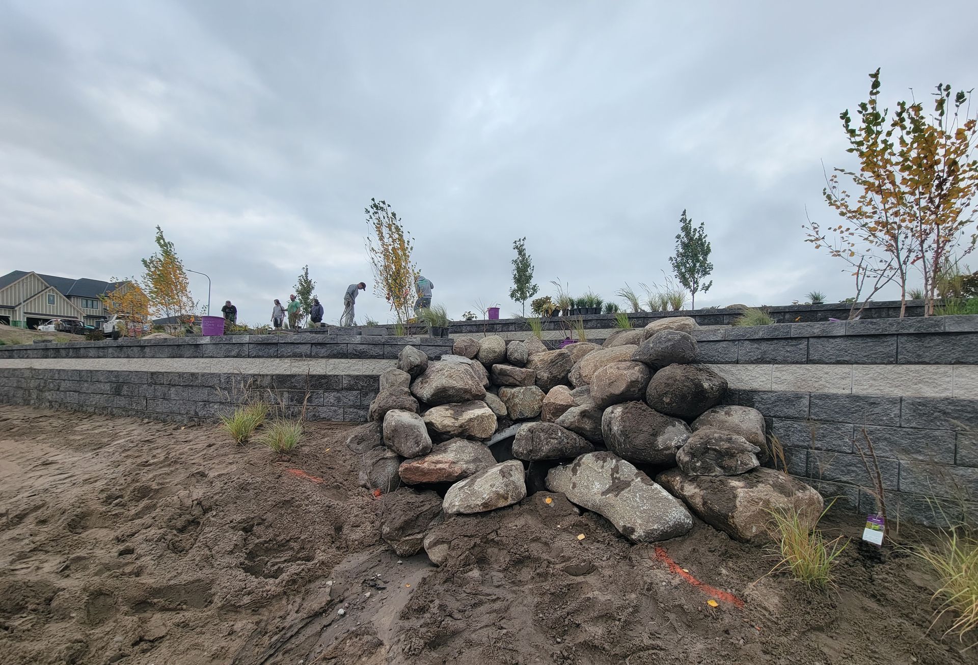 A pile of rocks sitting on top of a dirt field next to a brick wall.