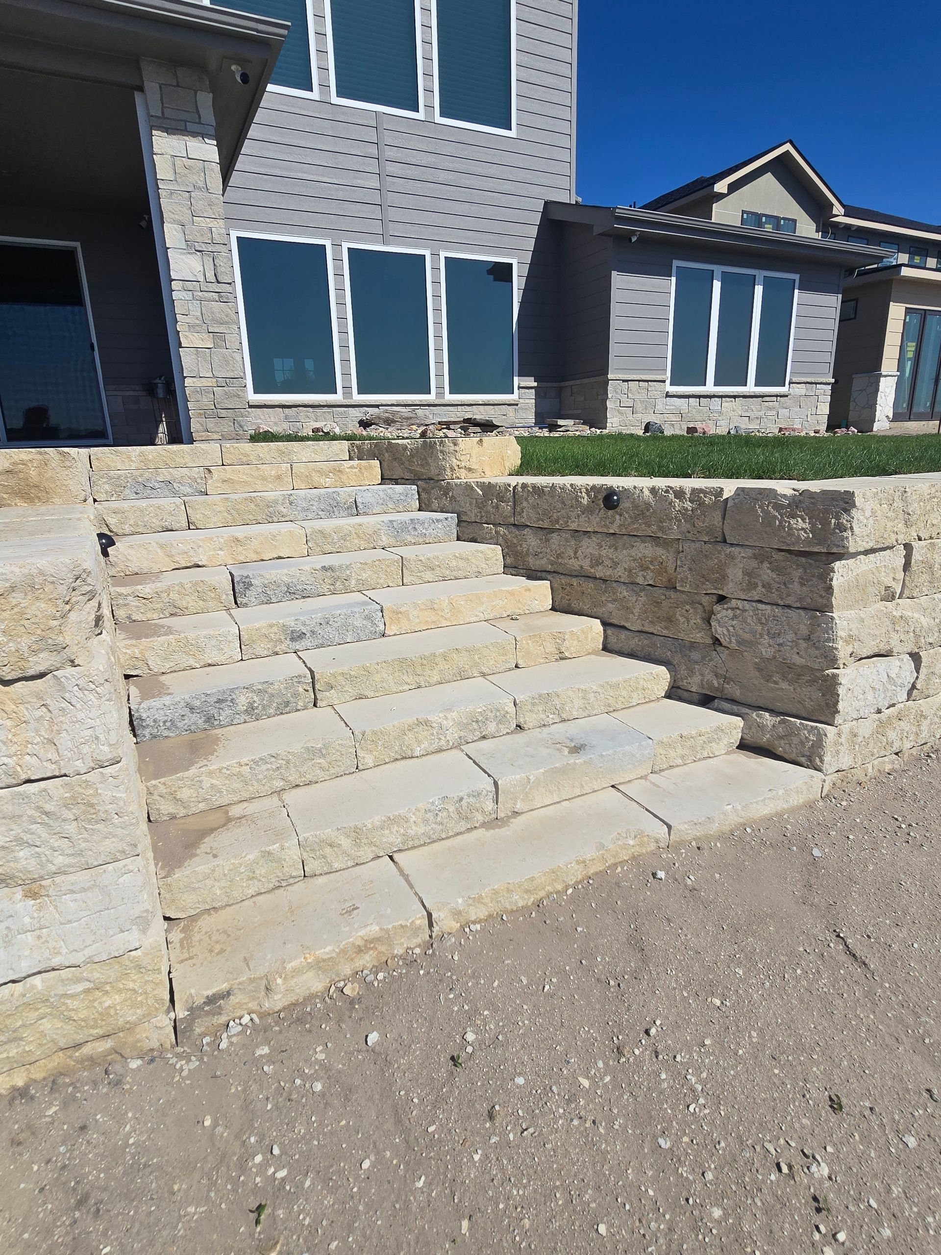 Stone steps leading up to the entrance of a modern house with stone siding and large windows.