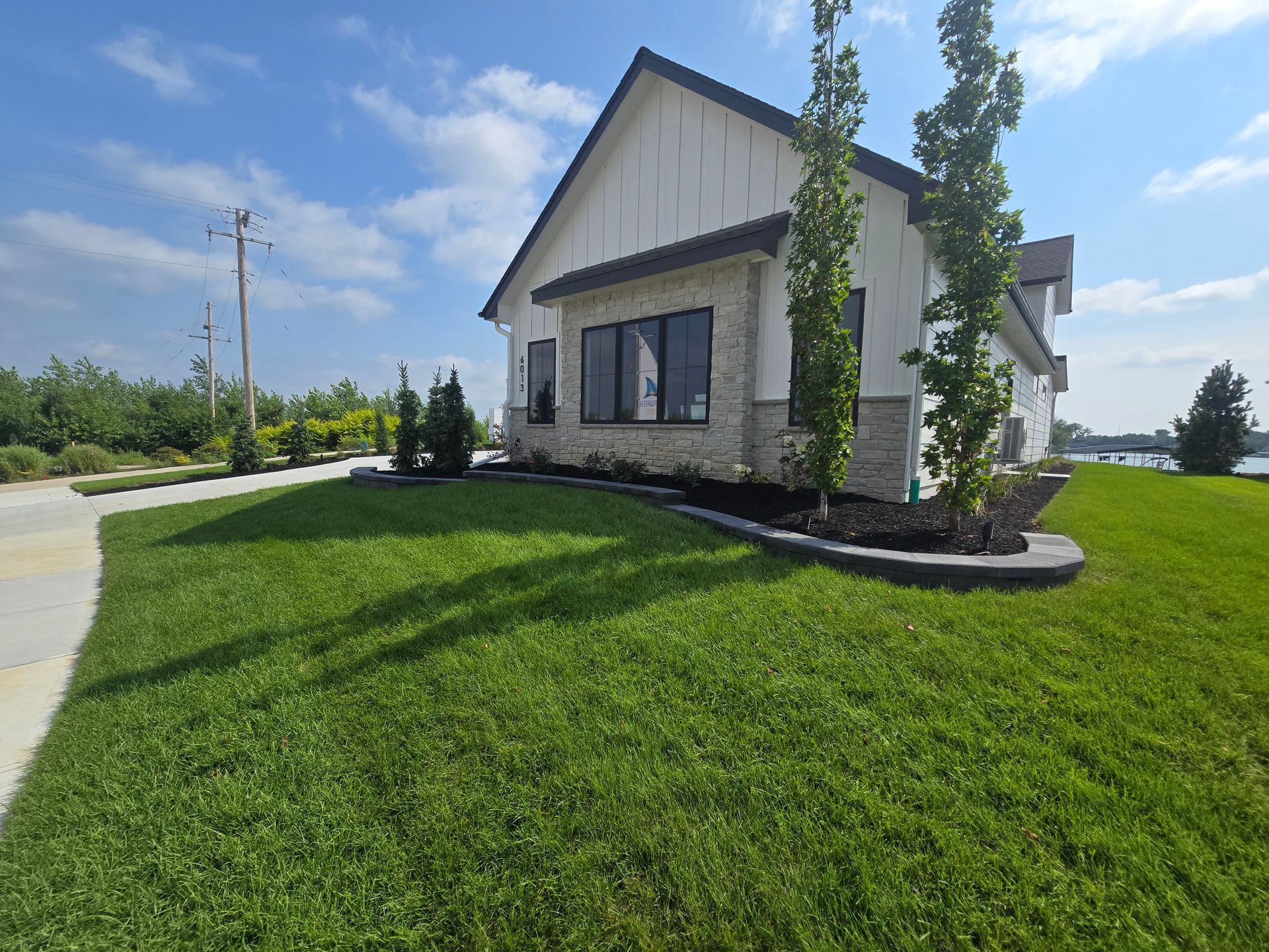 Modern white house with stone accents, lush green lawn, and blue sky.