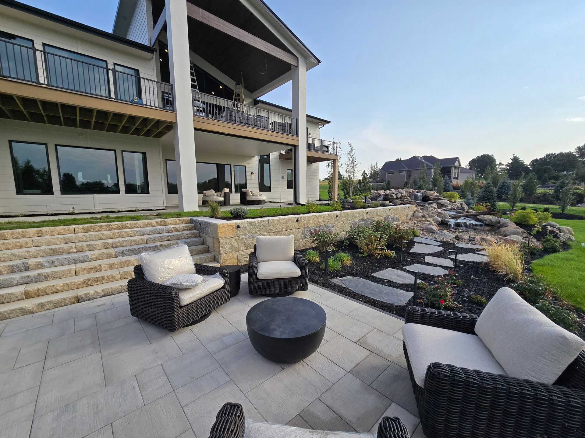 Patio with modern furniture in front of a large house with upper-level balcony.