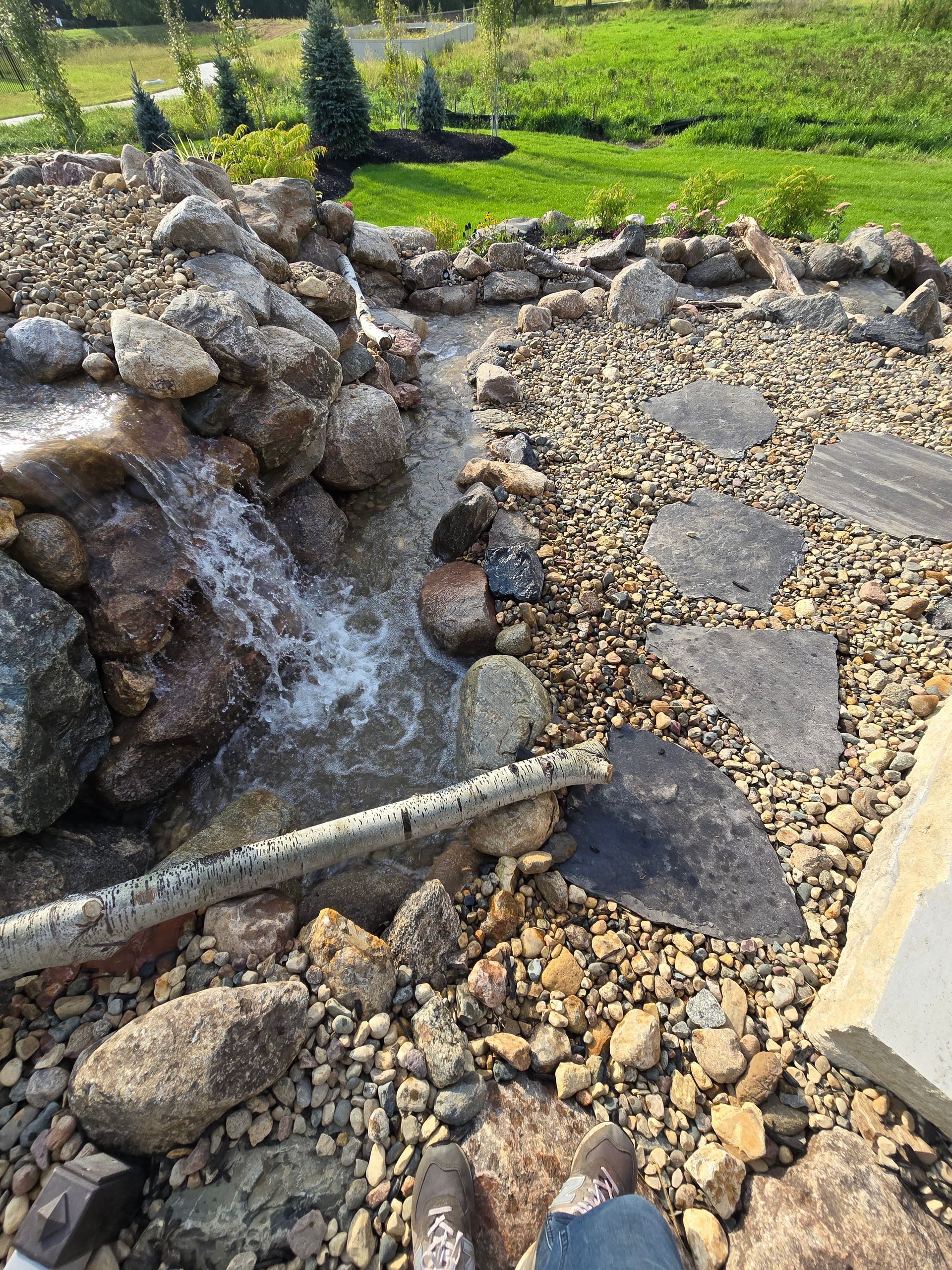 Water flowing over rocks with a log, creating bubbles.